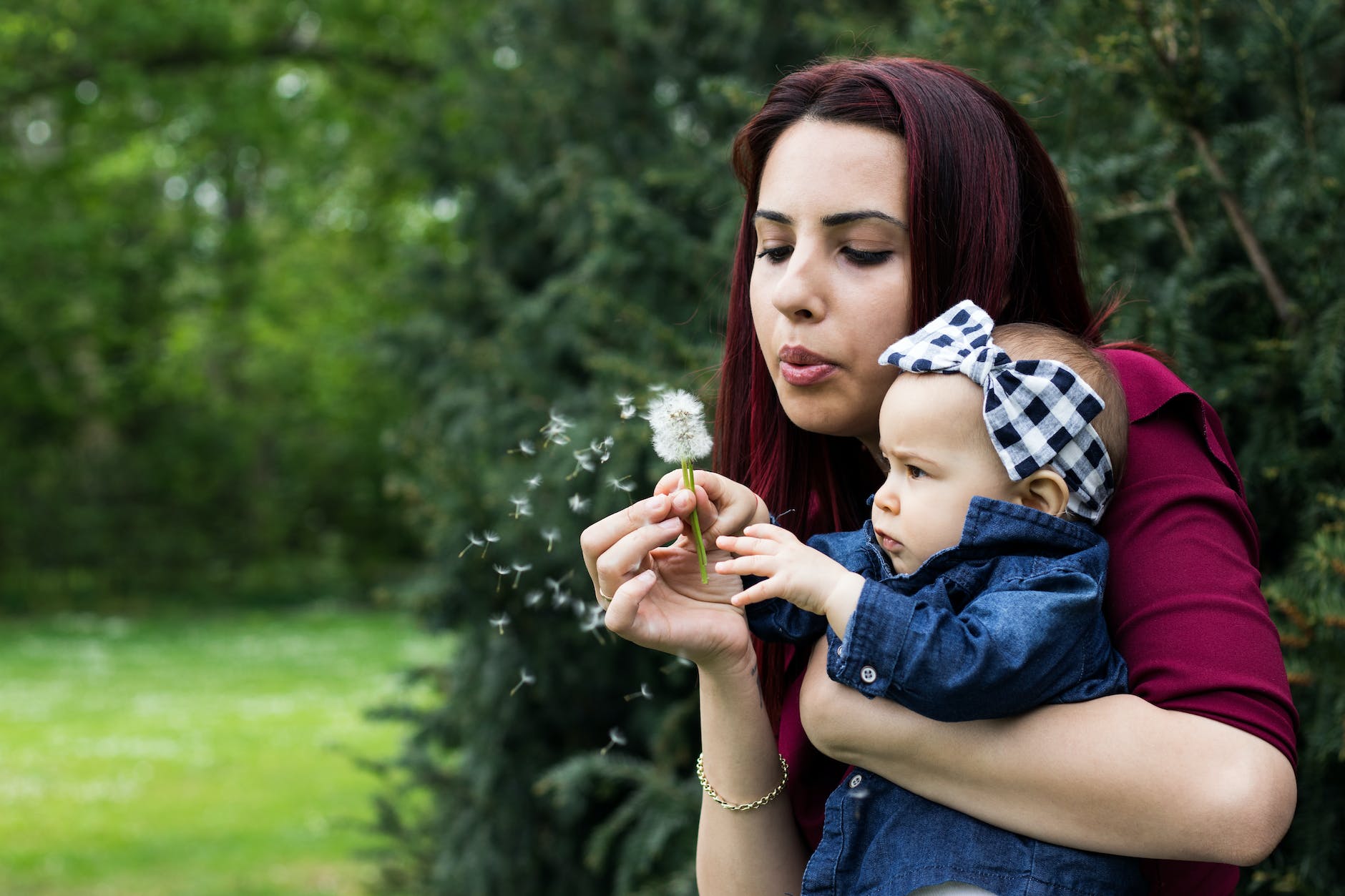 woman holding baby while blowing dandelion